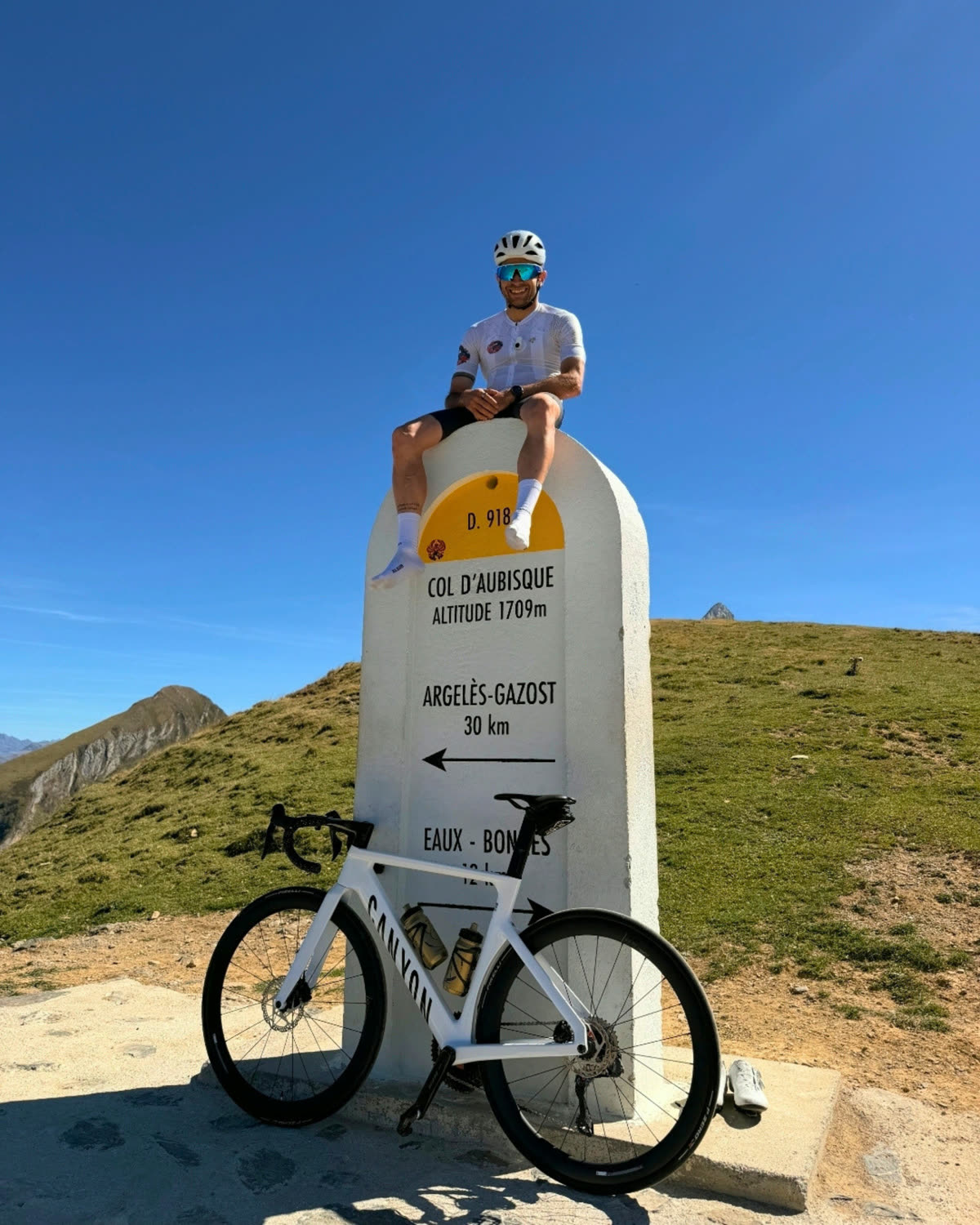 Rodrigo sitting on the Col d'Aubisque summit marker, his bike leaning below